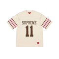 JeevzPlug Supreme cream short sleeve football jersey with studded detailing, brown graphic text, and striped sleeves.