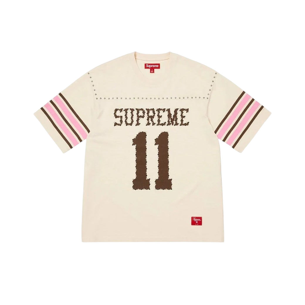 JeevzPlug Supreme cream short sleeve football jersey with studded detailing, brown graphic text, and striped sleeves.